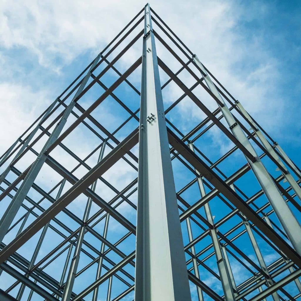 Steel framework of a building under construction, viewed from below against a blue sky with scattered clouds.